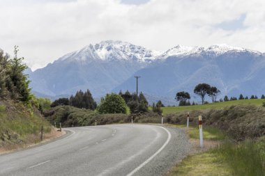 Yeşil yamaçta 94. yol kıvrımlı ve arka planda karlı zirveler, Te Anau, Southland, Güney Adası, Yeni Zelanda yakınlarındaki parlak bahar ışığında çekilen manzara