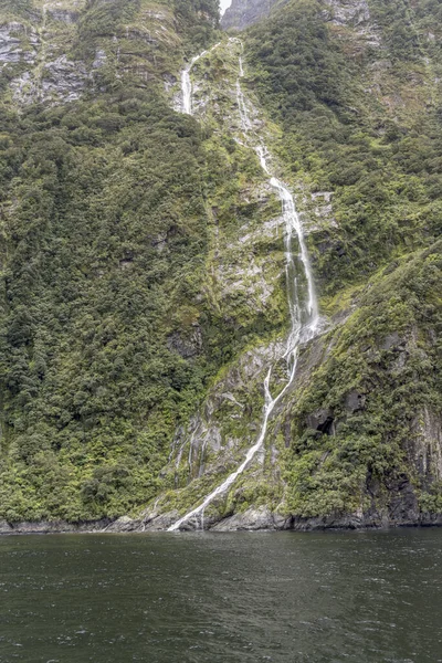 急な崖の上の滝と風景フィヨルドの海岸で顔 ミルフォードサウンドで曇った明るい光の中で撮影 ニュージーランド — ストック写真