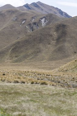Dağ yamaçlarında çorak yamaçlara sahip arazi, Lindis Geçidi yakınlarındaki parlak bahar ışığında çekildi, Otago, Güney Adası, Yeni Zelanda