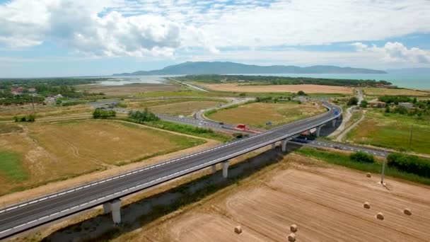 空中飞行越过田野 下公路 鸟瞰图 背景为蓝天白云和山脉 在田野上存放着一捆干草 旁边的公路 — 图库视频影像