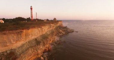 Gün batımında deniz korkunç taşlarla uçurumun havadan görünümü. Gün batımında uçurumun kenarında eski deniz feneri.