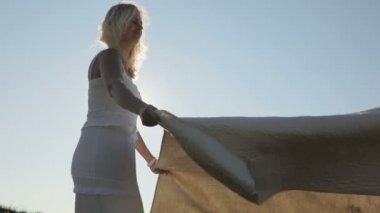 Gün batımında doğa yere bir örtü koyarak kadın. Ağır çekim.