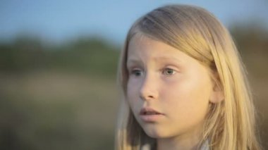 Küçük bir kız üzgün bir yüz ile ileri görünüyor. Gün batımı yakın çekim.
