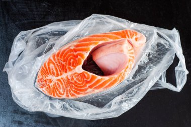 Siyah arka planda açık bir çantada büyük somon bifteği.