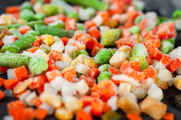 Farklı renkte donmuş sebzelerin bir karışımı bir taş standında yatıyor.