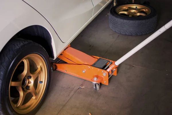 Car Lifted with orange hydraulic floor jack — Stock Photo, Image