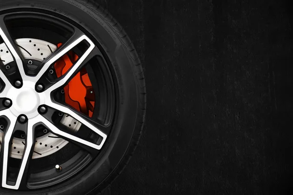 Alloy wheels of racing car with metal brake discs and red caliper on a black cement wall background. — Stock Photo, Image