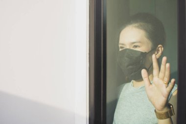 Enfeksiyona karşı maske takan Asyalı bir kız Coronavirus 'un yayılmasını engellemek için cam penceredeki eline dokunuyor..
