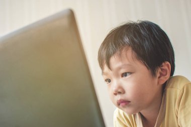 Asyalı küçük çocuk evde bir odada dizüstü bilgisayar ekranına bakarken sert ol..
