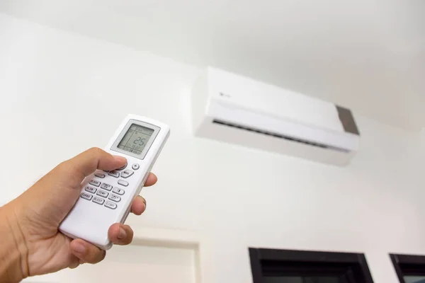 Human hand is using white remote of air conditioner for turn on and  adjust air conditioner in a room.