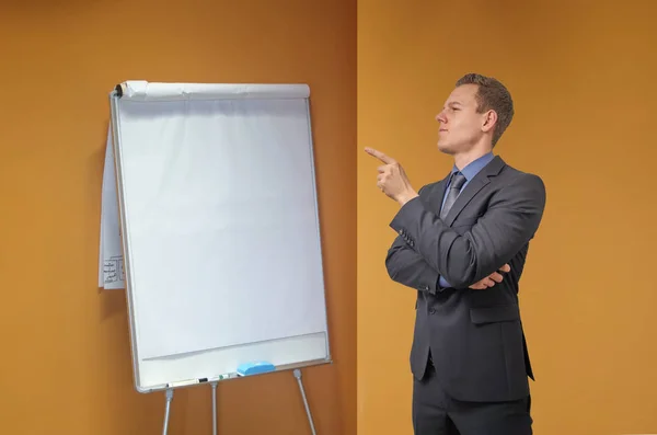 Young businessman points with his finger to a flip chart in the office - isolated with copyspace. Sceptical, critical or analyzing expression for advertisement. — Stock Photo, Image