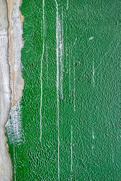 old concrete wall covered with textured plaster and painted with green paint. splashes of white paint and cracks, background for design