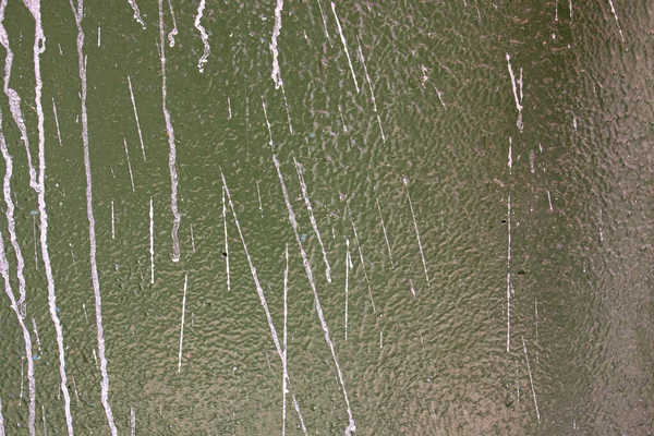 old concrete wall covered with textured plaster and painted with green paint. splashes of new white paint and cracks, background for design