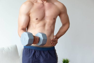 Atletik genç adam evdeki oturma odasında dambılla egzersiz yapıyor.