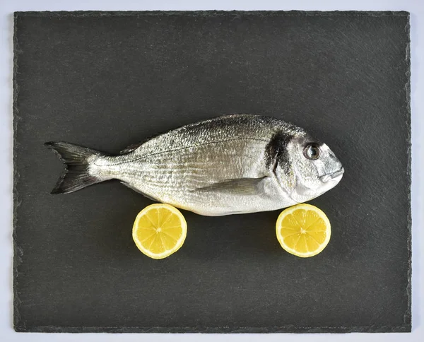 Un pesce orata crudo pronto da cuocere con limone su tavola di ardesia di pietra — Foto Stock