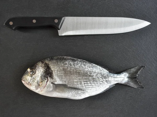 Один готовий до приготування сирої риби з ножем на кам'яному сланцевому кабані — стокове фото