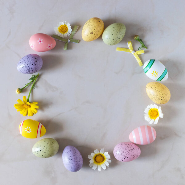 Creative Easter layout made of colorful eggs and flowers on marble background.