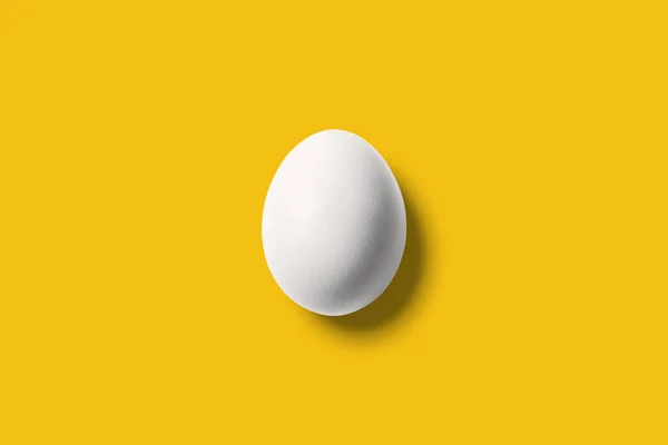 Ovo branco sobre fundo amarelo brilhante. Conceito mínimo . — Fotografia de Stock