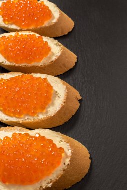 Koyu taşlı arka planda somon kırmızısı havyarlı sandviçler.