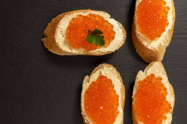 Koyu taşlı arka planda somon kırmızısı havyarlı sandviçler.