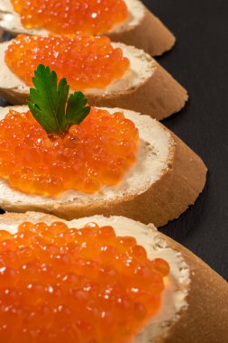 Koyu taşlı arka planda somon kırmızısı havyarlı sandviçler.