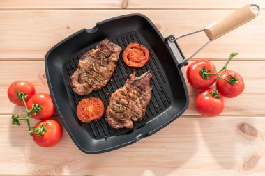 Ahşap zemin üzerine domatesli ızgara tava üzerinde ızgara biftek