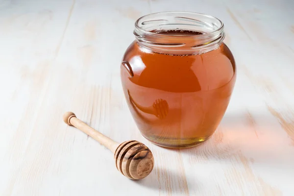 Μέλι σε βάζο σε ξύλινο υπόβαθρο και κουτάλα μελιού. — Φωτογραφία Αρχείου