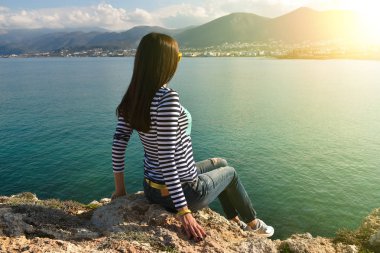 Güzel kız kayanın üzerinde oturur ve denizde görünüyor