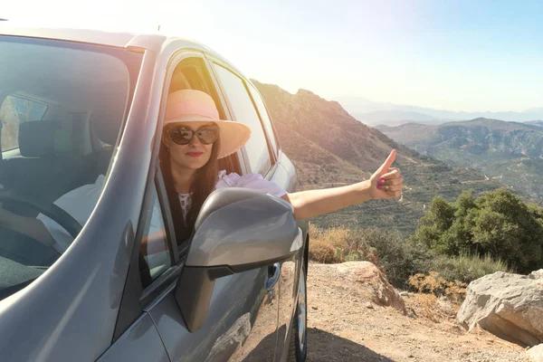Mujer feliz dentro de un coche conduciendo en la calle y señalando pulgar hacia arriba — Foto de Stock