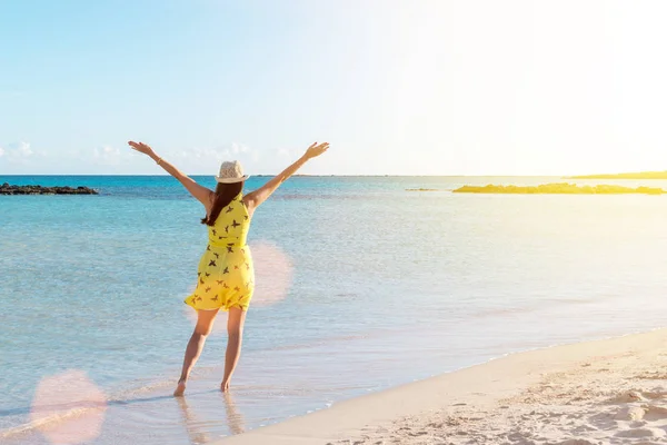 Gelukkig jonge vrouw in gele jurk met opgeheven handen op het strand — Stockfoto