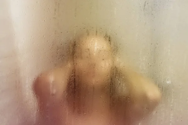 Hermosa mujer en la ducha detrás de vidrio con gotas. Brillo amarillo — Foto de Stock