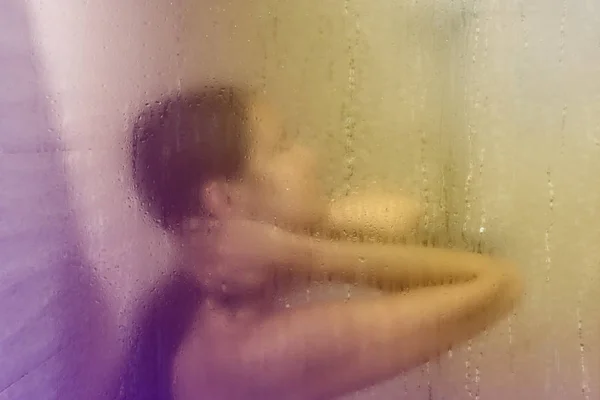 Beautiful woman in the shower behind glass with drops. Pink glow — Stock Photo, Image