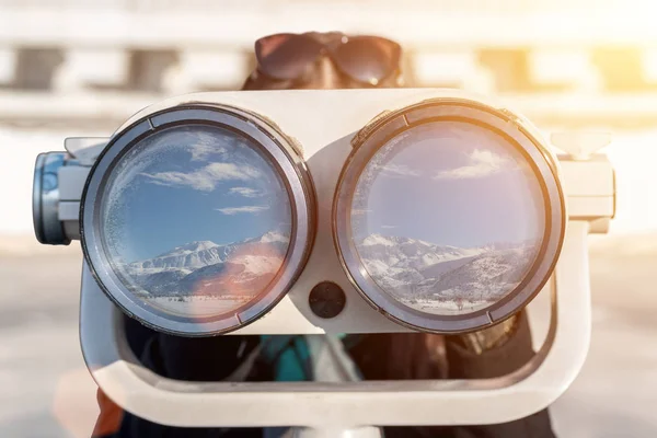 En kvinna ser ut genom kikare. I reflektion av glaset kan du se snö och bergen. — Stockfoto