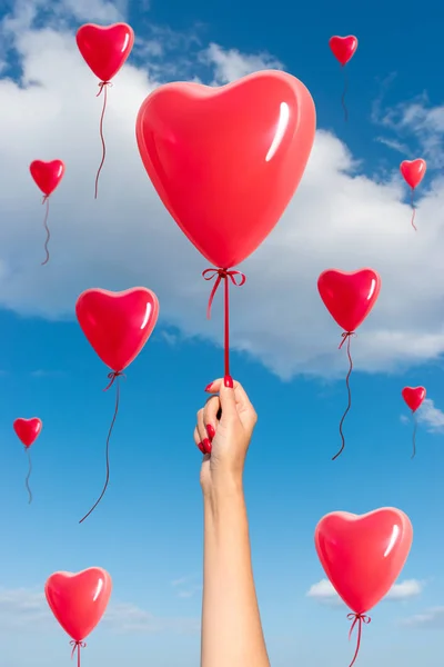 Womans hand with heart shaped balloons on background of sky.