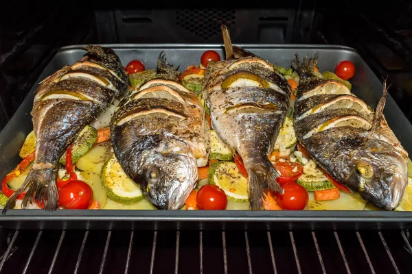 Roasted dorada fish with vegetables and lemon in the oven. — Stock Photo, Image