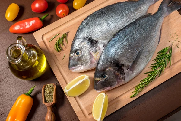 Fresh uncooked dorado or sea bream fish with lemon, herbs, oil, vegetables and spices — Stock Photo, Image