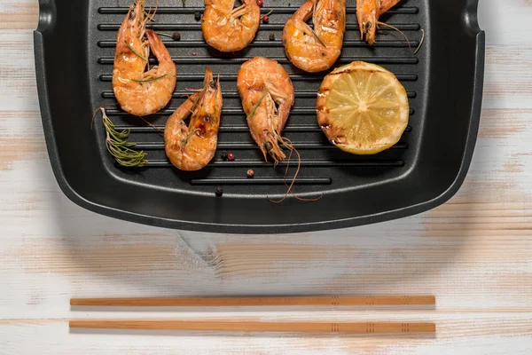 Grilled shrimp on a grill frying pan with lemon, paprika, spices and herbs.