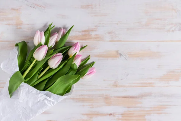 Tulipas cor-de-rosa embrulhadas em papel branco sobre fundo de madeira . — Fotografia de Stock