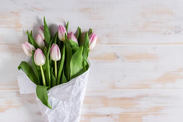 Tulipas cor-de-rosa embrulhadas em papel branco sobre fundo de madeira . — Fotografia de Stock