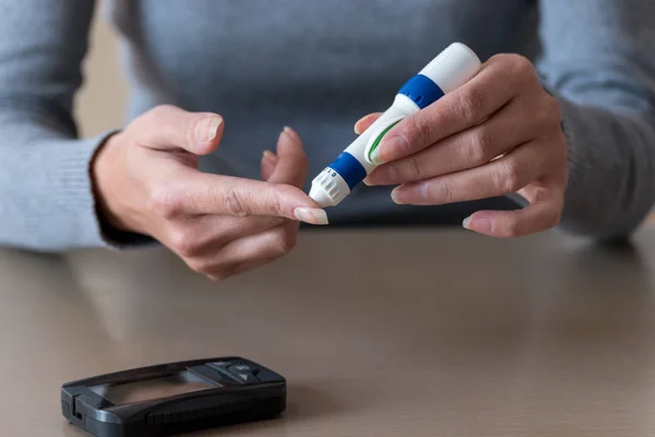 Närbild av kvinna händer använder lancet på finger för att kontrollera blodsockernivå av blodsockermätare. — Stockfoto