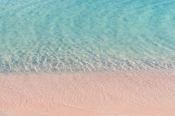 Soft waves of the sea on the pink sand and beautiful beach with cliffs.Coast of Crete island in Greece. Pink sand beach of famous Elafonisi