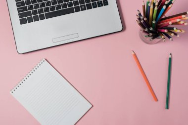 Dizüstü bilgisayar ve pembe bir arka plan üzerinde boş not defteri en az çalışma alanı.