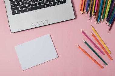 Dizüstü bilgisayar ve pembe bir arka plan üzerinde boş not defteri en az çalışma alanı.