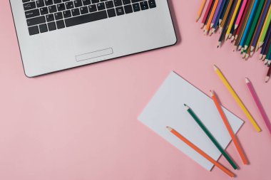 Dizüstü bilgisayar ve pembe bir arka plan üzerinde boş not defteri en az çalışma alanı.