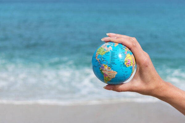 Human hand is holding small globe in front of the sea. 