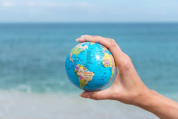 Человеческая рука держит маленький глобус перед морем. Концепция путешествий и глобальные проблемы . — стоковое фото