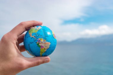 İnsan eli küçük küre mavi gökyüzü önünde tutuyor. 