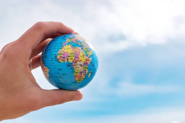 A mão humana está segurando um pequeno globo na frente do céu azul . — Fotografia de Stock