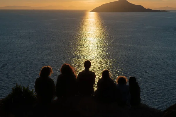 Sziluettjét az emberek figyel naplemente a tengerre és a sziklák. — Stock Fotó
