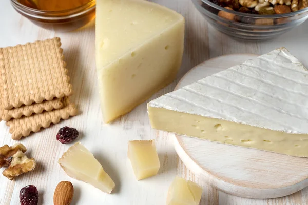 Queso Brie fresco, graviera de queso griego y una rebanada sobre tabla de madera blanca con nueces, miel y hierbas . —  Fotos de Stock